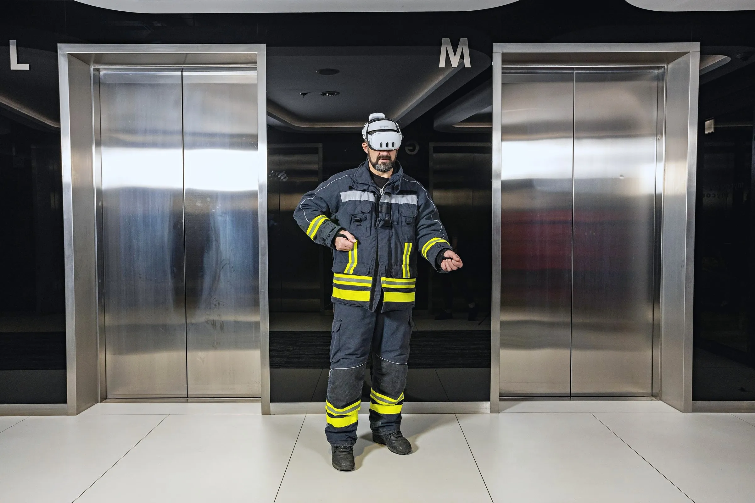 A firefighter in full turnout gear wearing a VR headset, standing between two lift doors