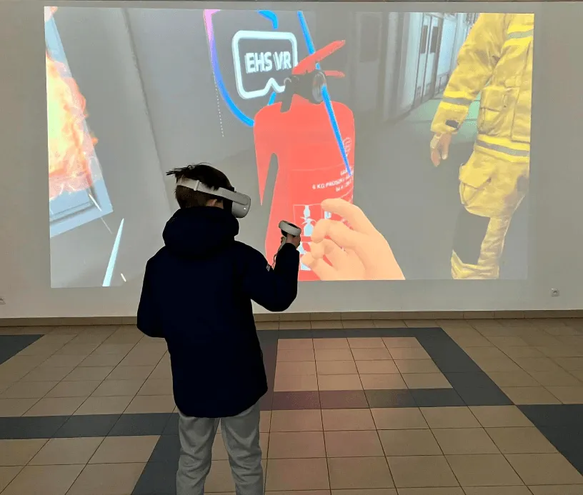 A child in a VR headset in front of a wall projection showing the VR fire safety scenario