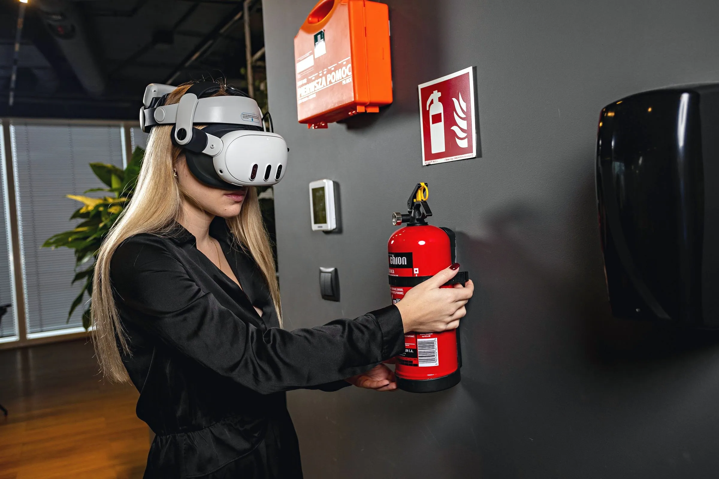 A woman in a VR headset reaching for a fire extinguisher mounted on a wall