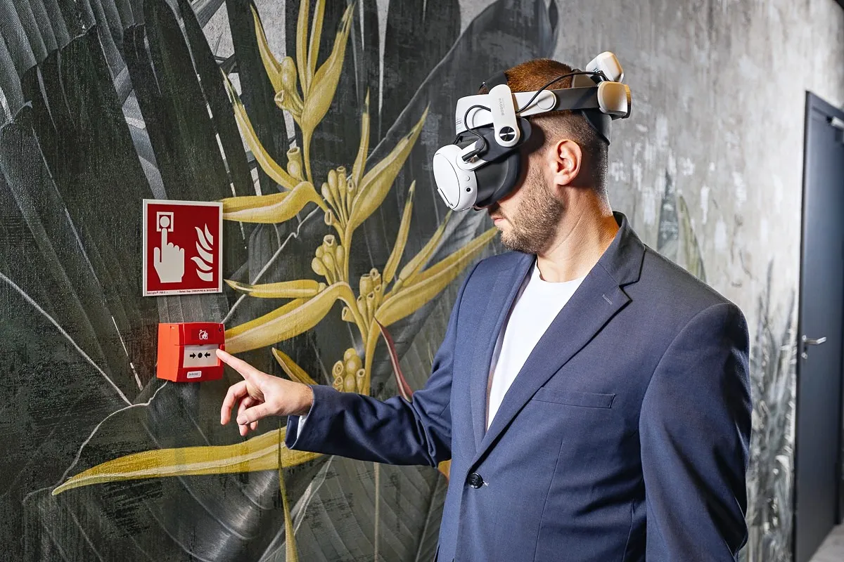 Un hombre con gafas VR pulsa un pulsador manual de alarma de incendio en la pared