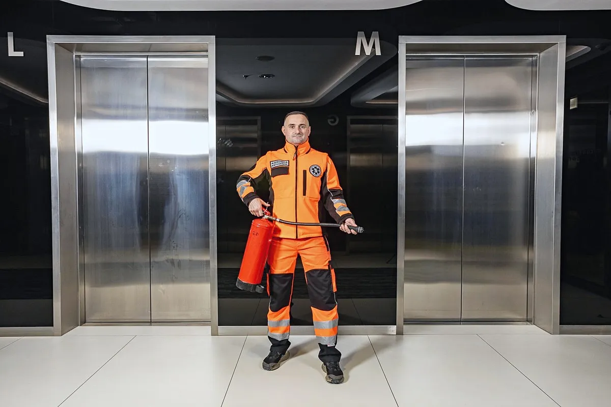 A rescuer in an orange suit holding a fire extinguisher by the elevators