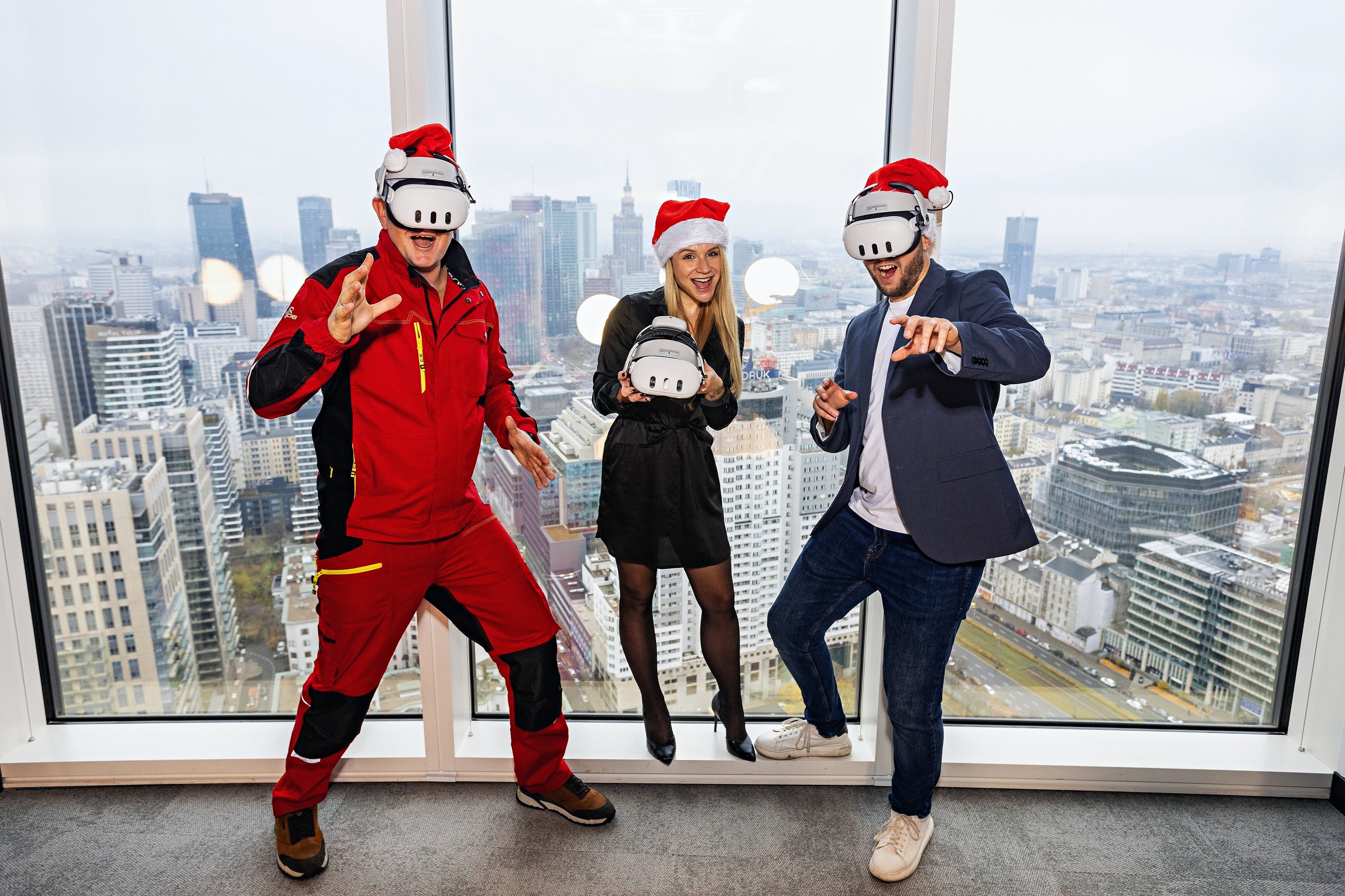 Three colleagues in Santa hats and VR headsets having fun by a window high above the city