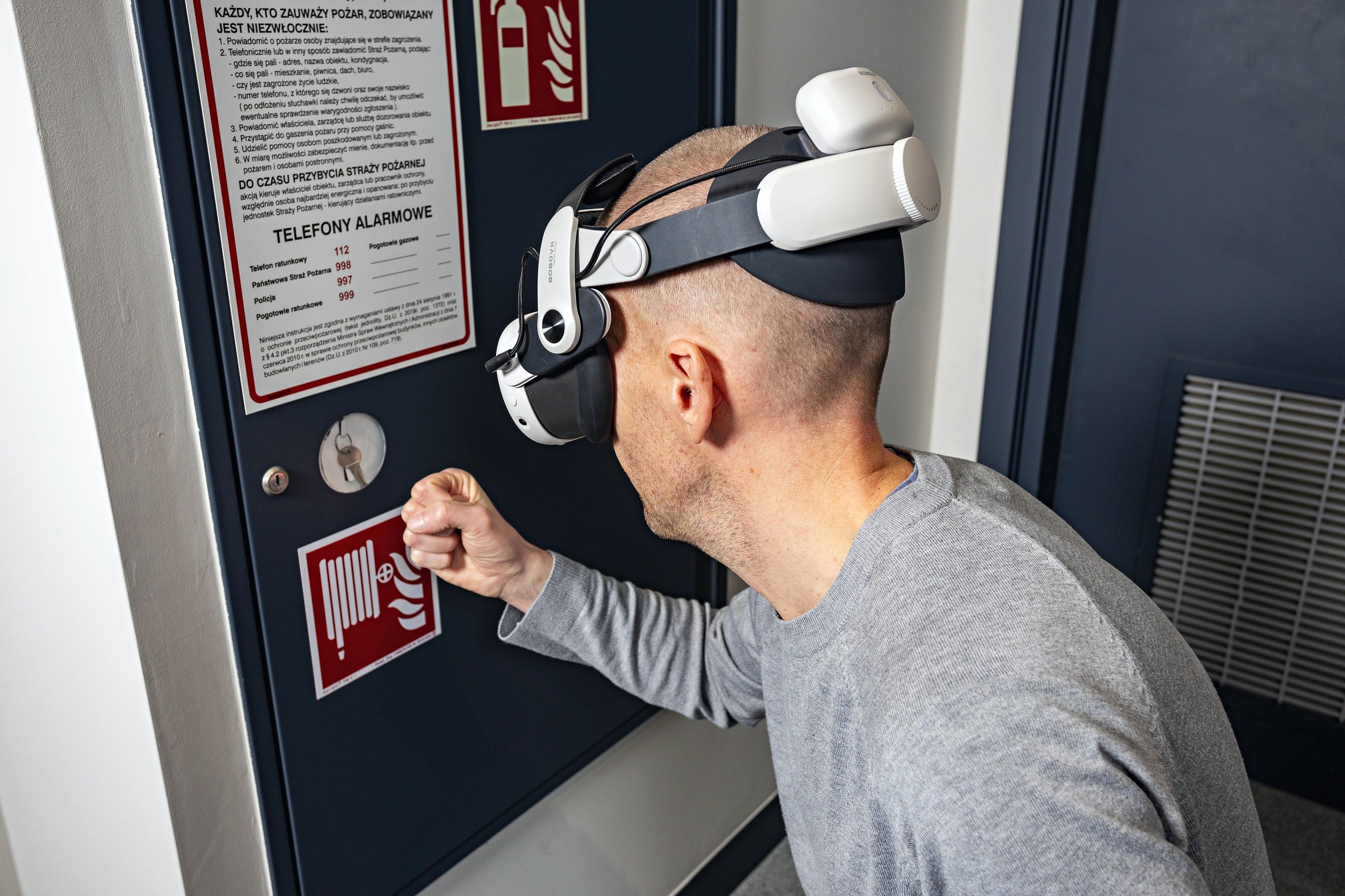 A trainee in a VR headset presses a manual fire alarm call point